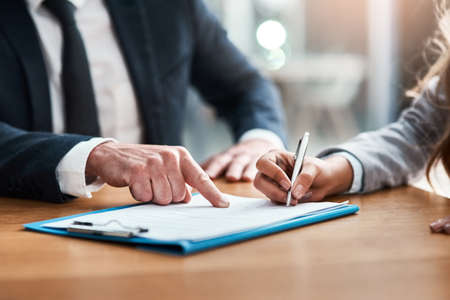 Please sign here if you agree to the terms. Closeup shot of two unrecognizable businesspeople going...
