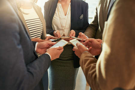 Business connections. a group of businesspeople using their cellphones while standing in a huddle.の写真素材