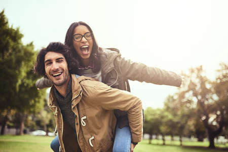 We are wild and free. Portrait of a cheerful young couple having a piggyback ride while looking at...