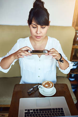 Posting this later. a beautiful young woman taking a picture of her coffee with a cellphone in a...