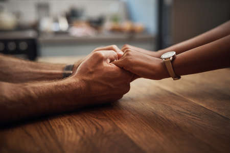 Couple holding hands in support, grief and healing together on a wooden table at home. Closeup of a caring partner in sorrow due to cancer and expressing feelings of compassion in a houseの写真素材