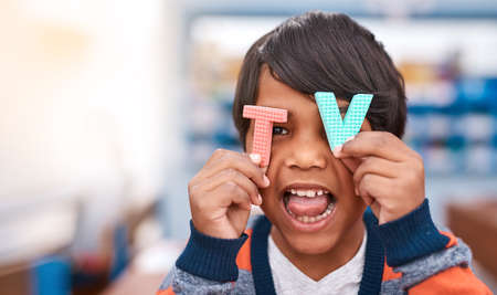 Mom always says I watch too much TV. a cheerful elementary school kid holding the letters T and V in front of his eyes inside of the classroom.の写真素材