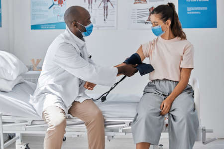 Doctor, medical and healthcare taking patient blood pressure at the hospital during covid pandemic. Health, consulting and worker helping woman with arm monitor for heart and healthy checkup.の写真素材