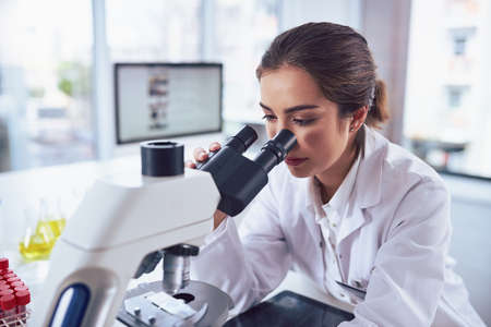 State of the art science equipment. a cheerful young female scientist looking through the lens of a microscope while being seated inside of a laboratory.の写真素材