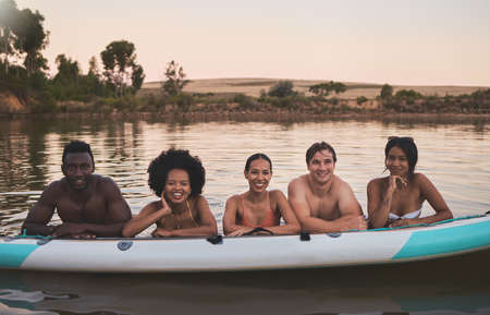 Diverse group of friends having fun while swimming at a lake in summer with a floating kayak boat....