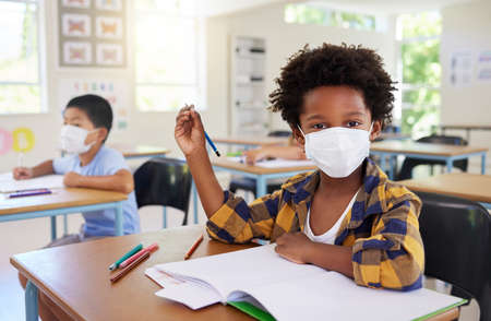 Child or student in class during covid, wearing a mask for hygiene and protection from coronavirus flu. Portrait kindergarten, preschool or elementary school boy sitting in a classroom ready to learnの写真素材