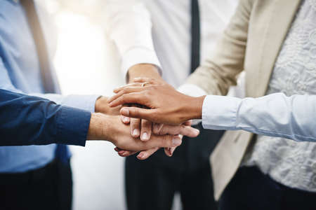 On three. an unrecognizable group of businesspeople standing in the office together with their hands...