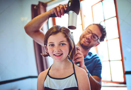 Dads my personal and favourite stylist. a father blowdrying his little daughters hair at home.の写真素材