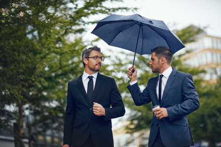 Heading off to their next meeting. two corporate businessmen travelling through the city on a rainy day.の写真素材
