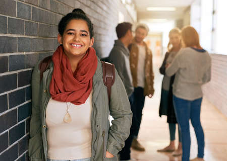 Im loving campus life. Portrait of a young female university student standing in a campus corridor with her classmates in the background.の写真素材