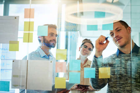Taking a creative approach to planning. a group of businesspeople brainstorming with notes on a glass wall in an office.の写真素材