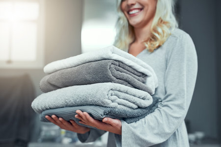 One stack of fresh laundry coming right up. Closeup shot of an unrecognizable woman carrying a pile of towels while doing laundry at home.の写真素材