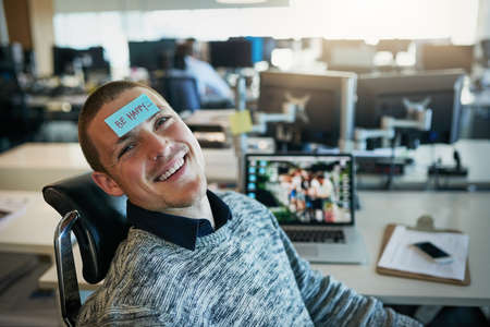 a cheerful young businessman with a sticky note on his forehead saying be happy while being seated...