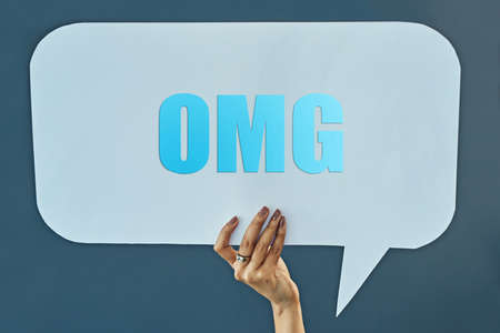 Speak out. Cropped studio shot of a woman holding up a speech bubble with a OMG on it against a gray background.の写真素材