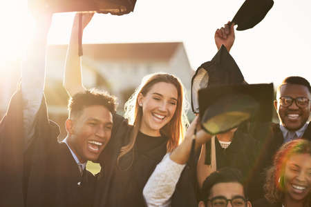 Today is our day. a group of smiling university students cheering and throwing their caps outside on graduation day.の写真素材