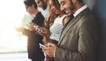 Connect with other businesses in your industry. businesspeople using their cellphones while standing in a row.の写真素材