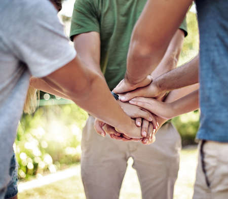 Theyre united. a young group of friends standing outside with their hands in a huddle.