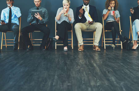 Its been a long wait. a group of well-dressed business people seated in line while waiting to be interview.の写真素材
