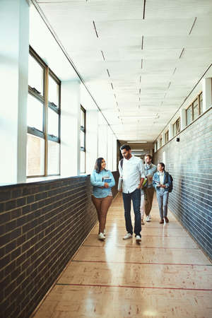 Headed to class. Full length shot of a group of university students walking through a campus corridor.の写真素材