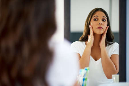I check everyday for any blemishes. an attractive young woman getting ready in her bathroom.の写真素材