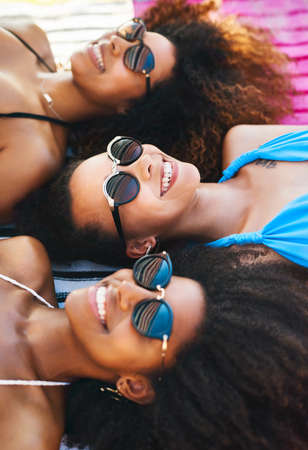 Beating the heat with the besties. a group of happy young women wearing sunglasses and relaxing at the beach.の写真素材