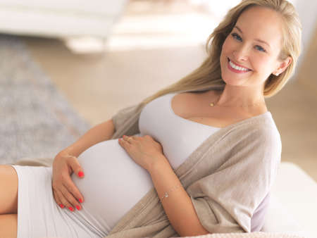 I finally get to be a mom. High angle portrait of a beautiful young pregnant woman sitting on the sofa at home.の写真素材