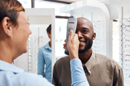 Eye exam, eyewear and an optometrist checking happy young male eyes with optic medical equipment. African man getting his eyesight checked by a tonometer. Smiling guy getting new spectacles.の写真素材