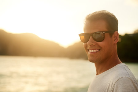 Being at the beach is my thing. Portrait of a handsome young man standing on the beach at sunset.の写真素材