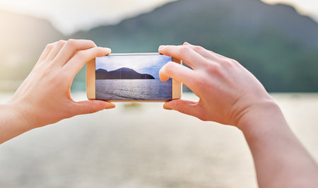 Happy holiday memories. an unidentifiable woman taking a picture with her smartphone while walking on the beach.の写真素材