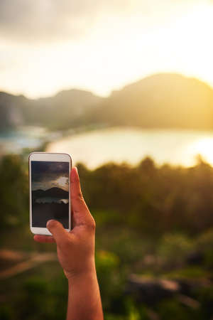 Take a bit of your holiday with you. an unidentifiable tourist using a smartphone to photograph an island view.の写真素材