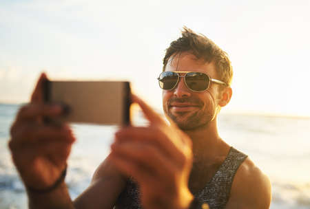 Capture every minute of summer. a young man taking a selfie at the beach.の写真素材