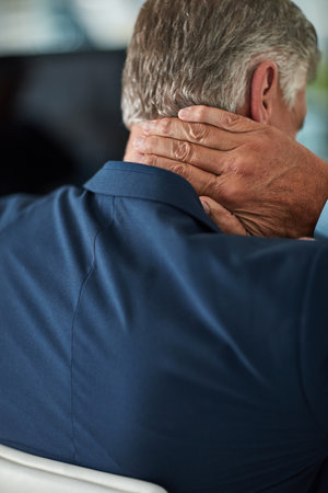 Feeling the strain. Rearview shot of a mature businessman rubbing his neck in the office.の写真素材