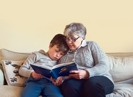Gran is the one always telling him so many stories. a grandmother reading a book to her grandson at home.の写真素材