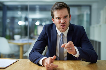 Youre fired. Portrait of an angry businessman shouting and pointing his finger while sitting at a desk.の写真素材