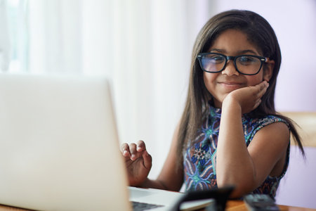 Clever cutie. Portrait of a cute little girl using a laptop in her bedroom at home.の写真素材