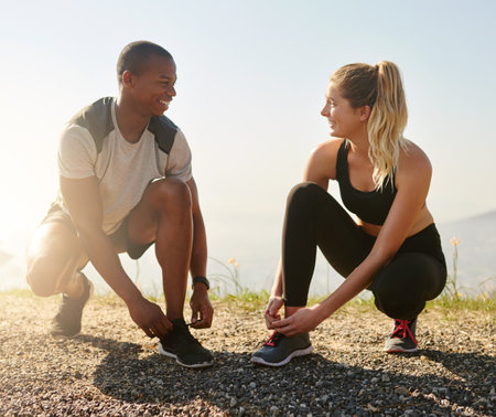 They share the same fitness goals. a fit young couple tying their shoelaces before a run outdoors.の写真素材