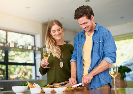 Spending quality time in the kitchen. a smiling young couple standing at their kitchen counter chopping up ingredients together for dinner.の写真素材