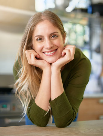 Happy and content at home. Portrait of a smiling young woman leaning on her kitchen counter at home.の写真素材