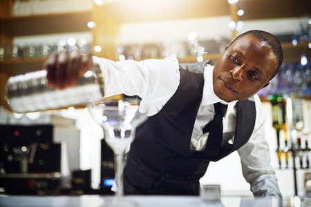 He makes the best cocktails. a well-dressed bartender standing behind the counter.