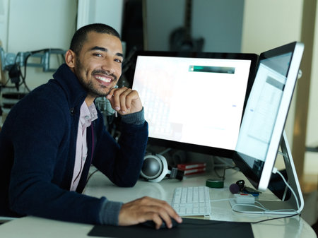 Ive got everything covered with this computer setup. Portrait of a smiling young man sitting at a desk working on a computer with dual monitors.の写真素材