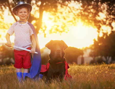 Were here to protect and serve. a little boy and his dog wearing capes while playing outside.の写真素材
