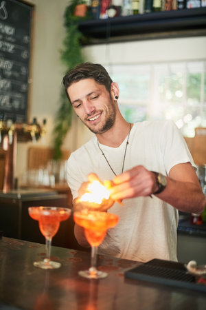 Whats life without a little flair. a happy young bartender lighting a cocktail on fire behind the...