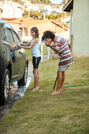 Having a quick drink of water before continuing. two cheerful children washing their parents car together outside during the day.の写真素材