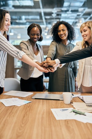 We got this guys. a cheerful group of businesspeople forming a huddle with their hands inside of the...