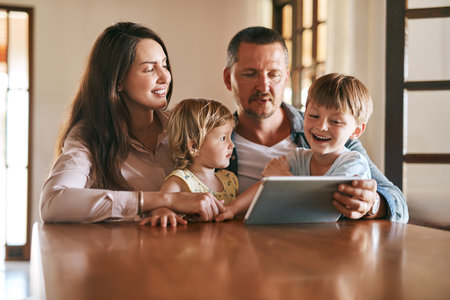Technology has its place in a modern home. a young family of four using a digital tablet together at home.の写真素材