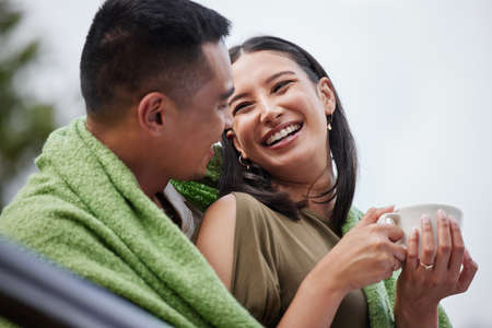 Cozy, smiling and romantic young couple cuddling and relaxing with blanket in cold winter. Loving husband and wife laughing and enjoying dating relationship bonding time in outdoors natureの写真素材
