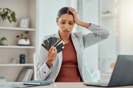 Financial stress, concerned and frustrated woman holding bank cards in her hand at her desk. Business female worried about economic decisions, credit interest or loan and debt in money crisis.の写真素材