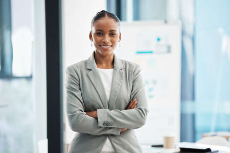 Proud, formal corporate businesswoman with arms crossed showing professional leadership, in marketing strategy presentation. Smiling employee standing in company boardroom for business meetingの写真素材