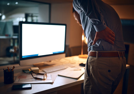Feels like I havent left my desk all day. Rear view shot of a young businessman suffering with back pain while working late in an office.の写真素材