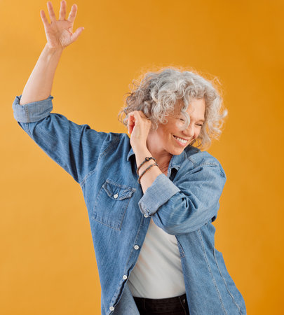 Celebrating, partying and dancing mature woman, happy and cheerful senior making waving hand gesture and smiling. Elderly caucasian woman having fun while she dances against an orange backgroundの写真素材